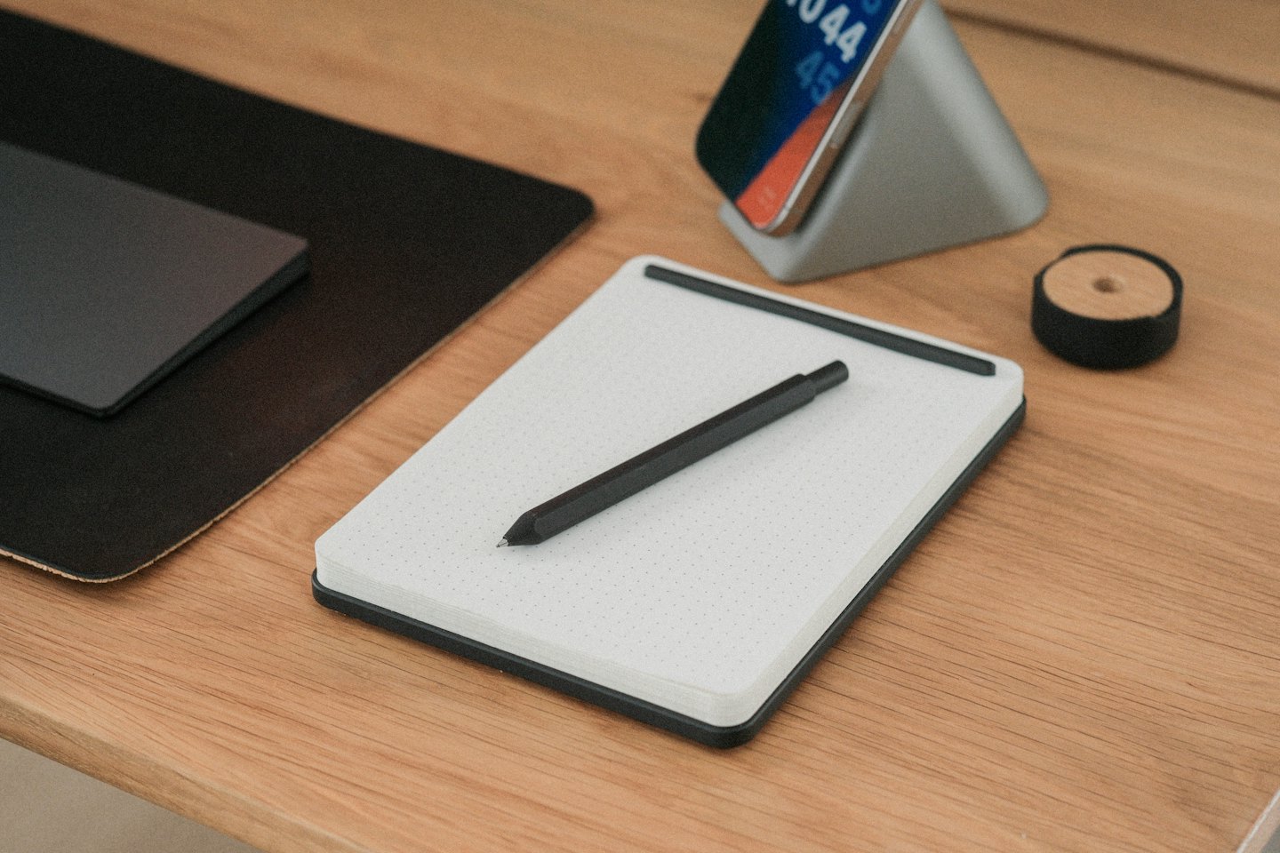 Scrivania minimalista con taccuino, smartphone e accessori.